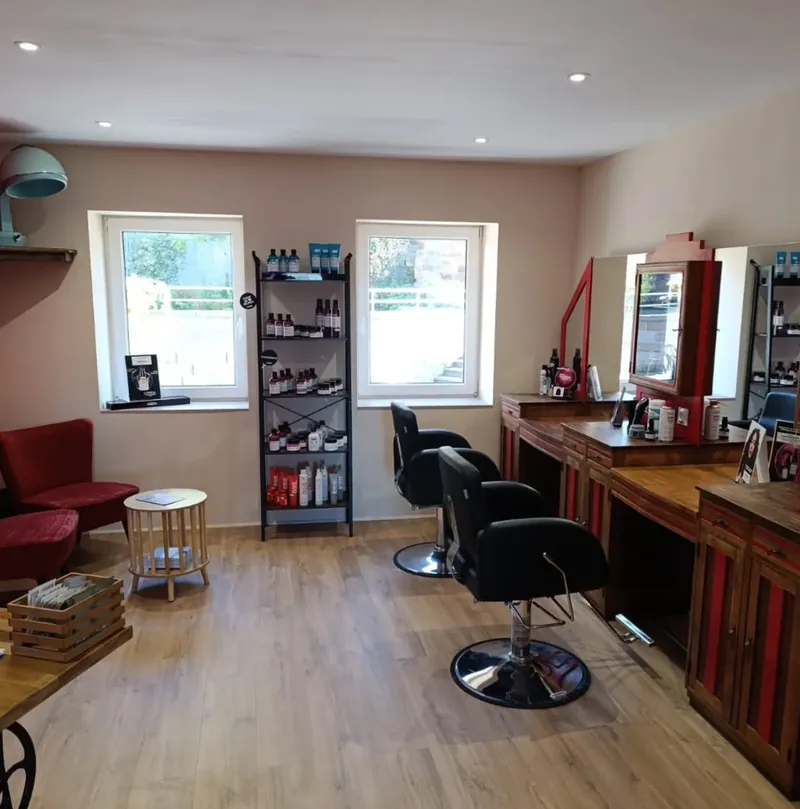 Espace du salon La Boucle Rouge à Œting : fauteuils rouges, présentoir de soins et postes de coiffage