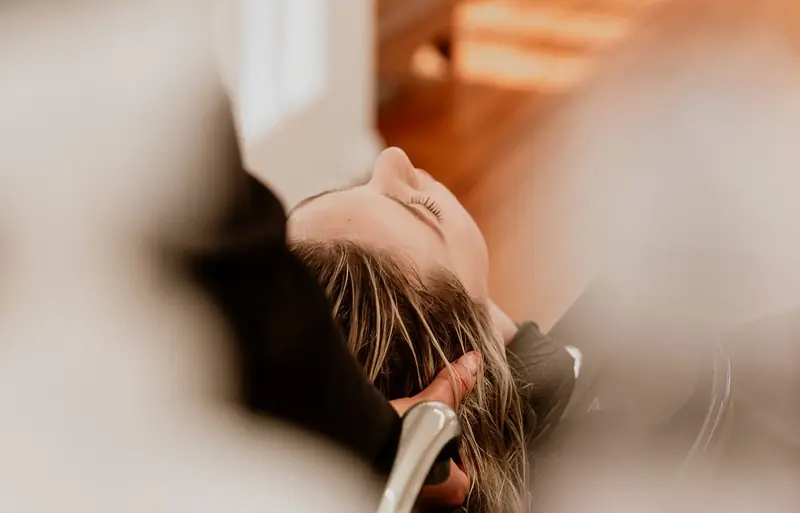 Cliente détendue, les yeux fermés, pendant un shampoing massant au bac
