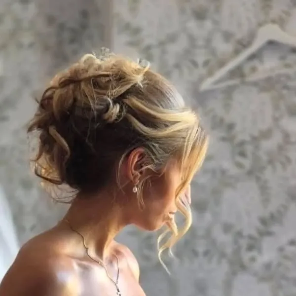 Détail d’un chignon de mariée bouclé avec mèches ondulées encadrant le visage