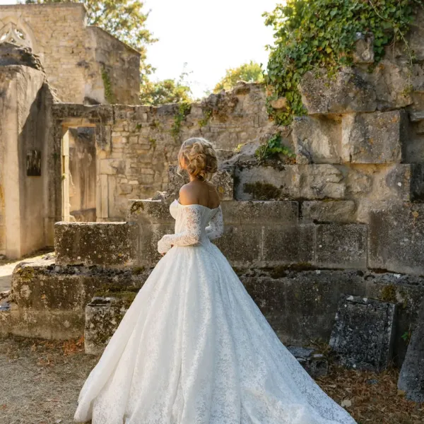 Mariée de dos en robe à traîne et chignon bouclé, dans un décor de vieilles pierres