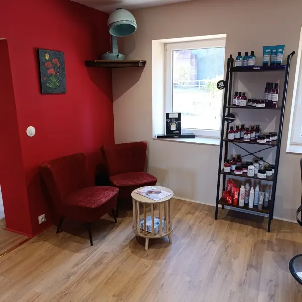 Coin d’attente du salon avec fauteuils rouges et produits professionnels
