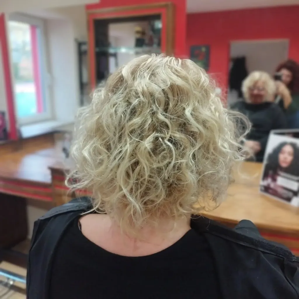 Cheveux blonds bouclés et courts après une coupe et un séchage naturel, vus de dos au salon